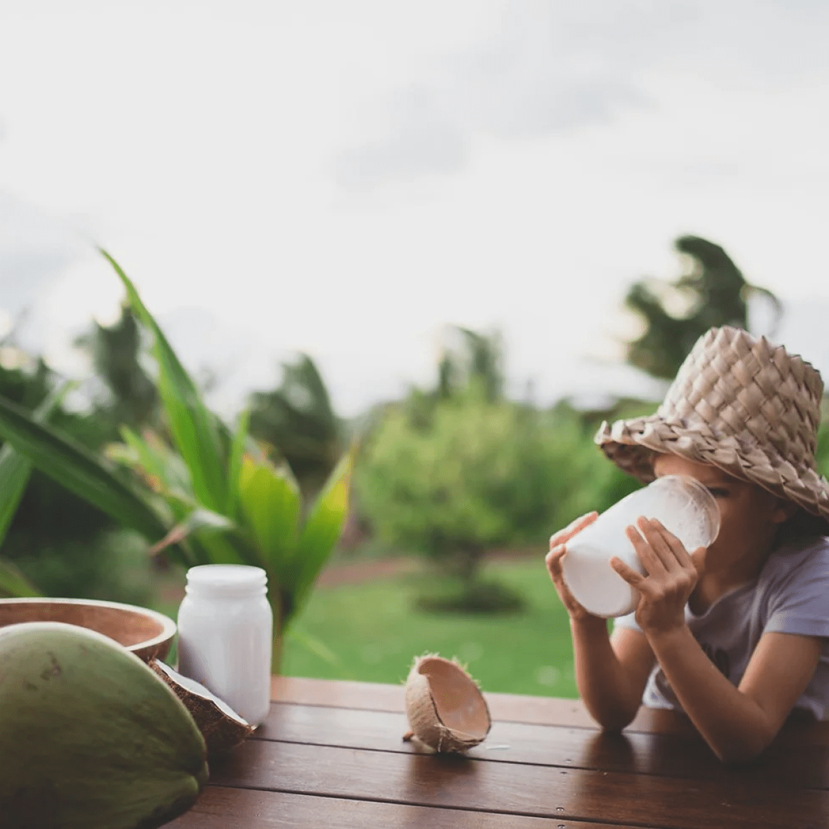 child sitting on a bench outside drinking a jar of coconut milk