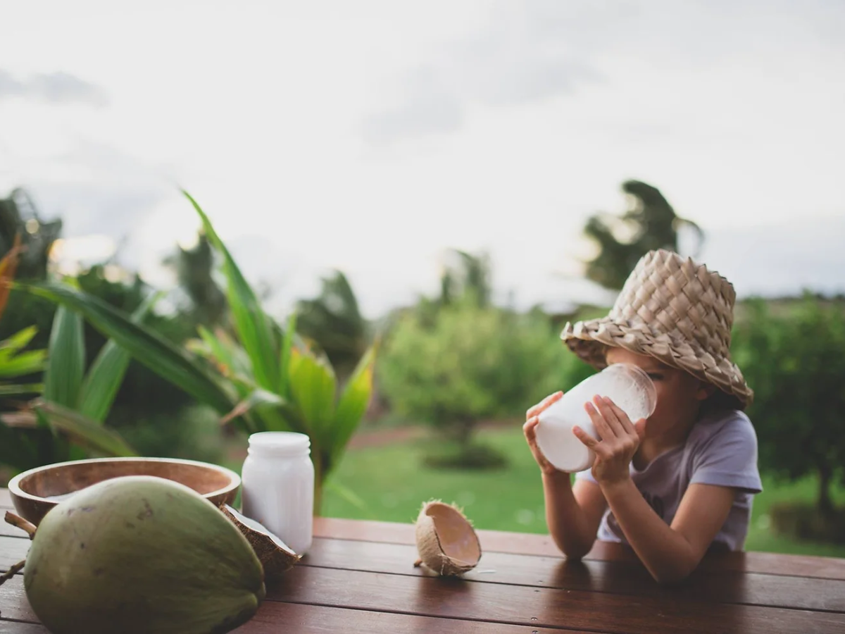 child sitting on a bench outside drinking a jar of coconut milk