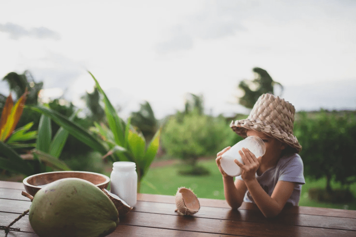 child sitting on a bench outside drinking a jar of coconut milk
