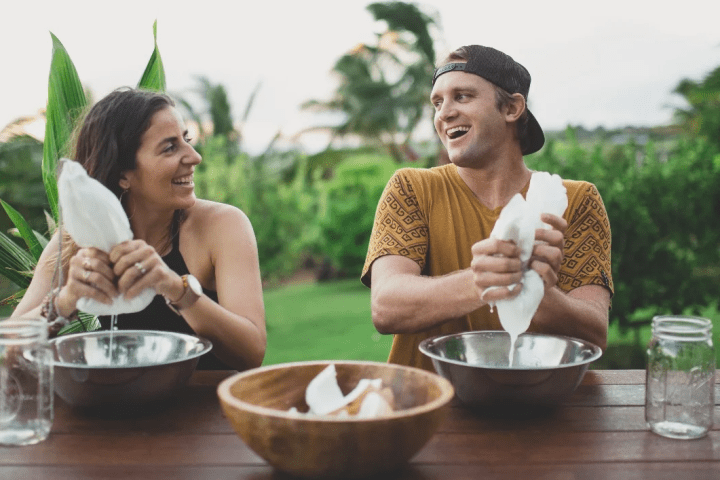 couple sitting at an outdoor table squeezing coconut milk into a bowl