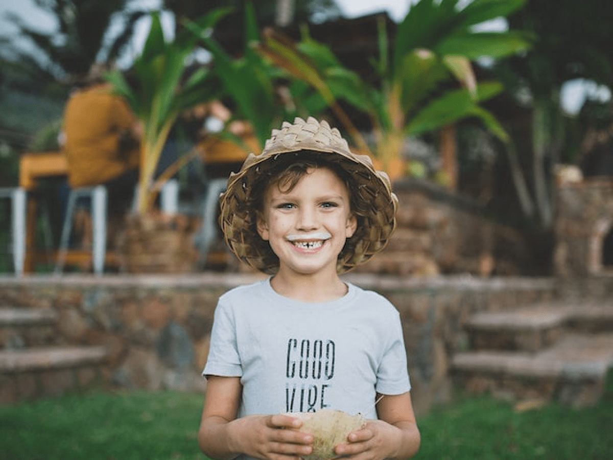 little boy in seagrass hat with a milk mustache holding half a coconut