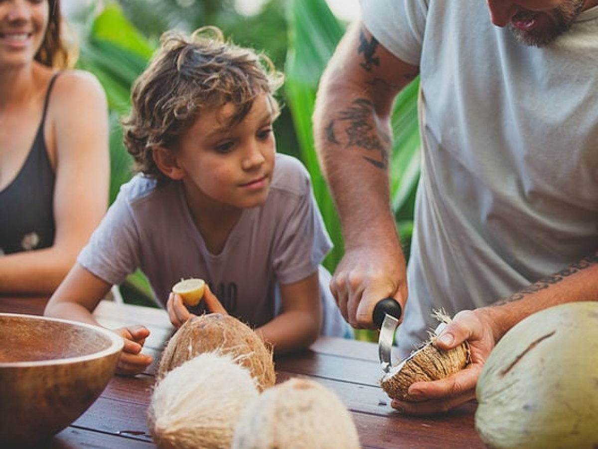 a woman and boy watching a man carve and harvest coconut meat