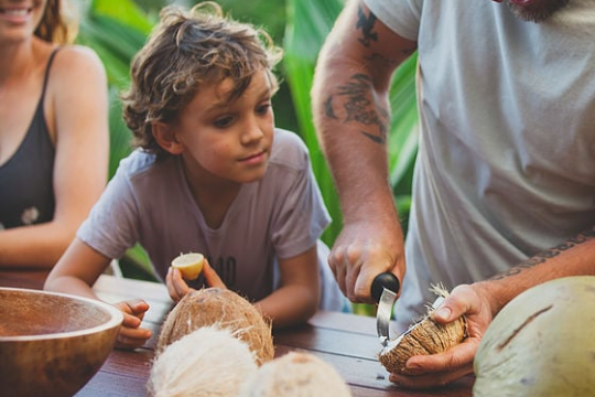 a woman and boy watching a man carve and harvest coconut meat